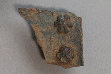 Fragment eines Blechs mit blütenförmigen Nieten aus Eisen von der Burg Mömbris, Unterfranken, letztes Drittel 14. Jh., Fd.-Nr. 020, H. 3,4 cm, Br. 3,4 cm